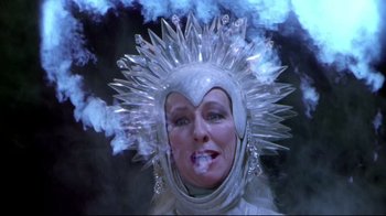 Movie still from “Masters of the Universe” (1987), directed by Gary Goddard – A woman in a white dress and a white head piece smoking a cigarette in front of smoke; Close Up shot, Low angle