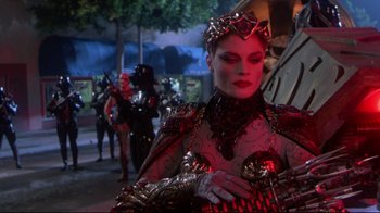 Movie still from “Masters of the Universe” (1987), directed by Gary Goddard – A woman dressed as a queen in a red outfit; Medium shot, Over the shoulder angle