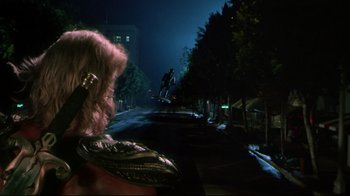 Movie still from “Masters of the Universe” (1987), directed by Gary Goddard – A man riding a skateboard down the side of a street; Wide shot, Over the shoulder angle