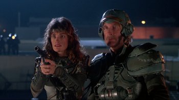 Movie still from “Masters of the Universe” (1987), directed by Gary Goddard – A man and a woman are standing next to each other holding guns; Medium shot, Low angle