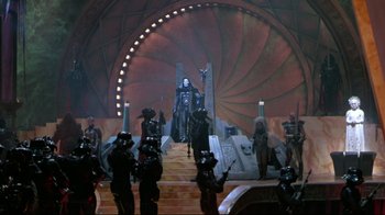 Movie still from “Masters of the Universe” (1987), directed by Gary Goddard – A group of people standing on top of a stage; Extreme Wide shot, Low angle