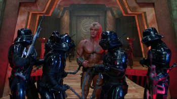 Movie still from “Masters of the Universe” (1987), directed by Gary Goddard – A group of people in a room with a man in the middle; Wide shot, Over the shoulder angle