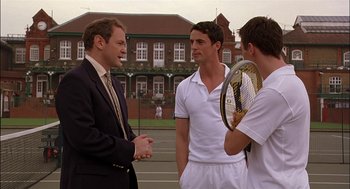 Movie still from “Match Point” (2005), directed by Woody Allen – Three men in suits talking to each other while holding tennis rackets; Medium shot, Over the shoulder angle