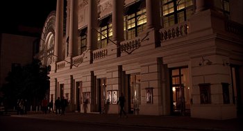 Movie still from “Match Point” (2005), directed by Woody Allen – People are walking on the sidewalk in front of a building at night; Extreme Wide shot, Low angle