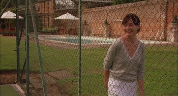 Movie still from “Match Point” (2005), directed by Woody Allen – A woman standing behind a chain link fence near a swimming pool; Wide shot, Over the shoulder angle