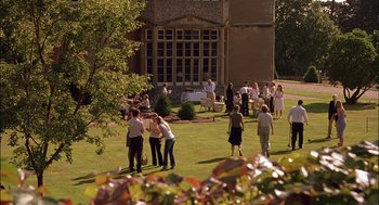 Movie still from “Match Point” (2005), directed by Woody Allen – A group of people standing in the grass near a building; Extreme Wide shot, High angle