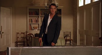 Movie still from “Match Point” (2005), directed by Woody Allen – A man in a suit standing next to a table; Medium shot, Low angle