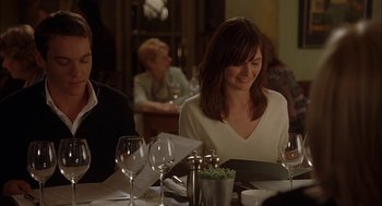Movie still from “Match Point” (2005), directed by Woody Allen – A woman sitting at a dinner table with wine glasses on the table; Medium shot, Over the shoulder angle