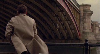 Movie still from “Match Point” (2005), directed by Woody Allen – A man in a tan coat standing in front of a building; Wide shot, High angle