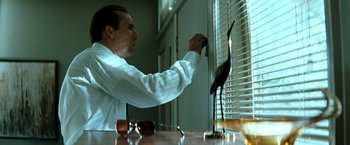 Movie still from “Matchstick Men” (2003), directed by Ridley Scott – A man in a white dress shirt and white tie looking out a window; Medium shot, Low angle