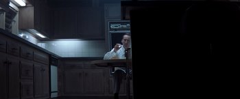 Movie still from “Matchstick Men” (2003), directed by Ridley Scott – A man sitting at a table in front of an oven in a kitchen; Medium shot, Low angle
