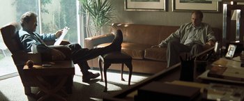 Movie still from “Matchstick Men” (2003), directed by Ridley Scott – A man sitting on a chair in a living room; Wide shot, High angle