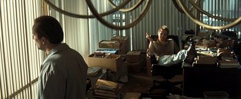Movie still from “Matchstick Men” (2003), directed by Ridley Scott – A man sitting on a chair in a room with boxes; Medium shot, Over the shoulder angle