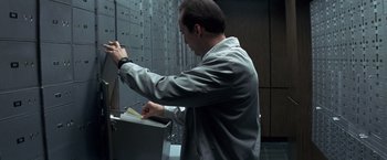 Movie still from “Matchstick Men” (2003), directed by Ridley Scott – A man is putting papers into a filing cabinet; Medium shot, Low angle