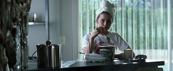 Movie still from “Matchstick Men” (2003), directed by Ridley Scott – A woman with a towel on her head sitting at a table with an ice cream container in front of her; Medium shot, High angle