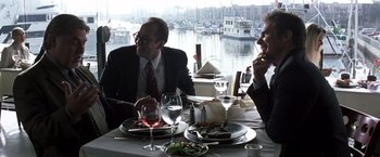Movie still from “Matchstick Men” (2003), directed by Ridley Scott – Two men sitting at a table with a plate of food; Medium shot, Over the shoulder angle