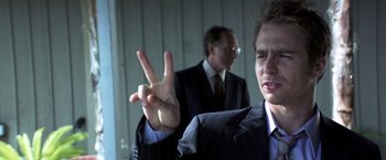 Movie still from “Matchstick Men” (2003), directed by Ridley Scott – A man in a business suit holding up a peace sign; Close Up shot, Low angle