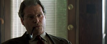 Movie still from “Matchstick Men” (2003), directed by Ridley Scott – An older man smoking a cigarette while wearing a suit; Close Up shot, Low angle