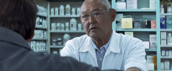 Movie still from “Matchstick Men” (2003), directed by Ridley Scott – An older man wearing glasses and a white lab coat; Close Up shot, Over the shoulder angle