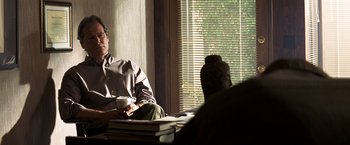Movie still from “Matchstick Men” (2003), directed by Ridley Scott – A man sitting at a table with a cup of coffee; Medium shot, Over the shoulder angle