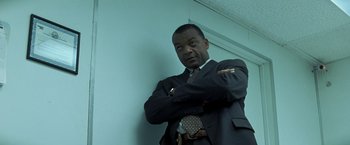 Movie still from “Matchstick Men” (2003), directed by Ridley Scott – A man in a suit and tie standing in front of a wall; Medium shot, Low angle