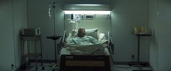Movie still from “Matchstick Men” (2003), directed by Ridley Scott – A man laying in a hospital bed in a room; Medium shot, Overhead angle