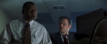 Movie still from “Matchstick Men” (2003), directed by Ridley Scott – A man in a suit and tie next to a man smoking a cigarette; Medium shot, Low angle