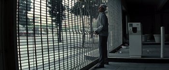Movie still from “Matchstick Men” (2003), directed by Ridley Scott – A man standing in front of a metal fence; Wide shot, Low angle