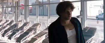 Movie still from “Matchstick Men” (2003), directed by Ridley Scott – A man standing in front of a window with chairs in the background; Medium shot, Low angle