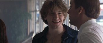 Movie still from “Matchstick Men” (2003), directed by Ridley Scott – A young man smiling at another young man in front of a window; Close Up shot, Over the shoulder angle