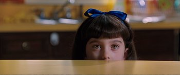 Movie still from “Matilda” (1996), directed by Danny DeVito – A little girl sitting at a table with a blue bow on her head; Close Up shot, High angle