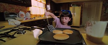 Movie still from “Matilda” (1996), directed by Danny DeVito – A little girl in the kitchen cooking pancakes; Medium shot, Overhead angle