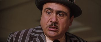 Movie still from “Matilda” (1996), directed by Danny DeVito – An older man with a mustache wearing a hat; Close Up shot, Over the shoulder angle