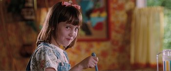 Movie still from “Matilda” (1996), directed by Danny DeVito – A little girl with a bow in her hair holding something; Close Up shot, High angle