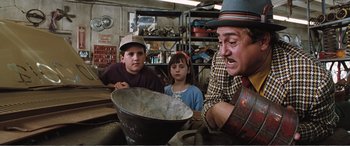Movie still from “Matilda” (1996), directed by Danny DeVito – Three children and an older man in a workshop; Medium shot, Over the shoulder angle
