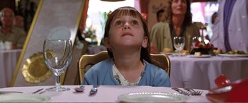 Movie still from “Matilda” (1996), directed by Danny DeVito – A little girl sitting at a dinner table looking up; Close Up shot, Low angle