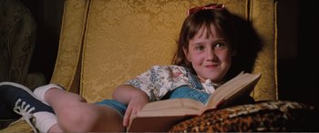 Movie still from “Matilda” (1996), directed by Danny DeVito – A little girl sitting on a couch reading a book; Close Up shot, High angle