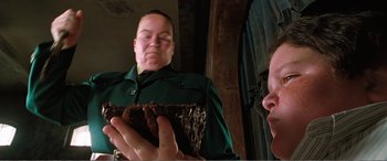 Movie still from “Matilda” (1996), directed by Danny DeVito – A man holding a piece of cake in front of a mirror; Close Up shot, Over the shoulder angle