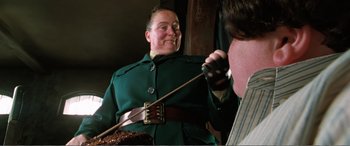 Movie still from “Matilda” (1996), directed by Danny DeVito – A man in a green coat is holding a sword; Medium shot, Low angle