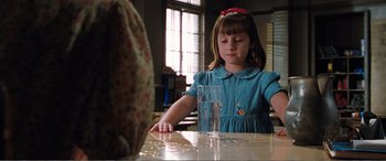 Movie still from “Matilda” (1996), directed by Danny DeVito – A little girl sitting at a table with a glass of water; Medium shot, Over the shoulder angle