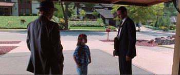 Movie still from “Matilda” (1996), directed by Danny DeVito – A little girl standing next to a man in a business suit; Wide shot, Over the shoulder angle
