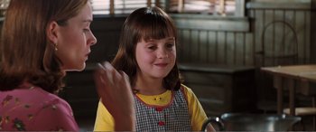 Movie still from “Matilda” (1996), directed by Danny DeVito – A young girl in a yellow shirt is smiling at the camera; Close Up shot, Over the shoulder angle