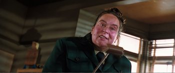 Movie still from “Matilda” (1996), directed by Danny DeVito – A woman in a green jacket is speaking to a microphone; Close Up shot, Low angle