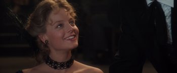 Movie still from “Maverick” (1994), directed by Richard Donner – A woman wearing a black choker smiling at the camera; Close Up shot, Over the shoulder angle