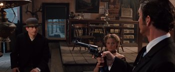 Movie still from “Maverick” (1994), directed by Richard Donner – A woman holding a gun in a room with chairs; Medium shot, Over the shoulder angle