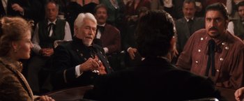 Movie still from “Maverick” (1994), directed by Richard Donner – An older man sitting in front of a group of people; Medium shot, Over the shoulder angle