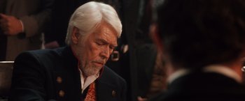 Movie still from “Maverick” (1994), directed by Richard Donner – An older man with white hair wearing a black suit and a red tie; Close Up shot, Over the shoulder angle