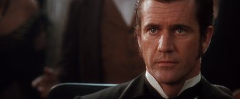 Movie still from “Maverick” (1994), directed by Richard Donner – A man in a suit and tie sitting in a chair; Close Up shot, Over the shoulder angle