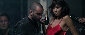 Movie still from “Max Payne” (2008), directed by John Moore – A man and a woman standing next to each other in front of a bottle; Close Up shot, Over the shoulder angle