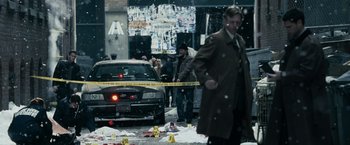 Movie still from “Max Payne” (2008), directed by John Moore – A man in a trench coat is standing next to a car; Wide shot, High angle